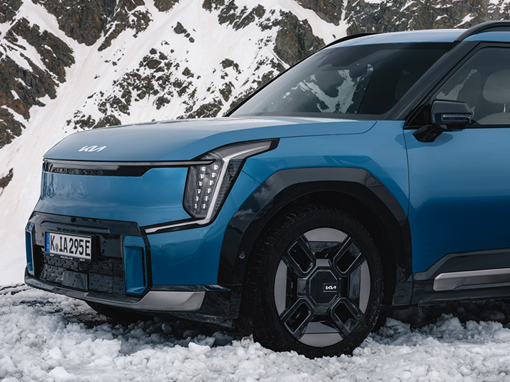 Blauer Kia SUV mit moderner Frontansicht, auf schneebedecktem Terrain mit Bergen im Hintergrund.