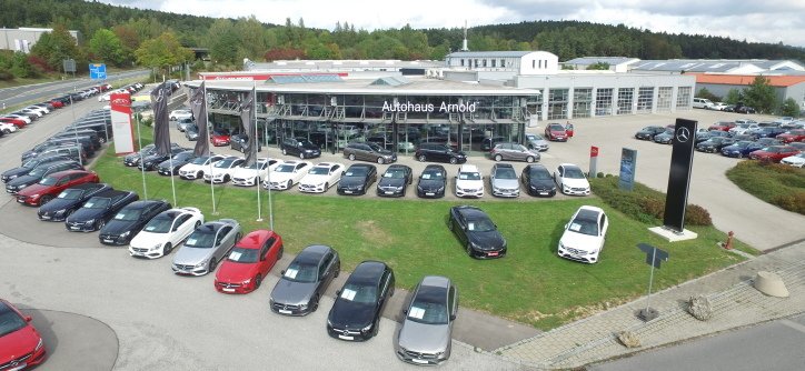 Autohaus Arnold mit einer Vielzahl von Autos im Freien in einer grünen Umgebung, im Hintergrund ein modernes Gebäudedesign.